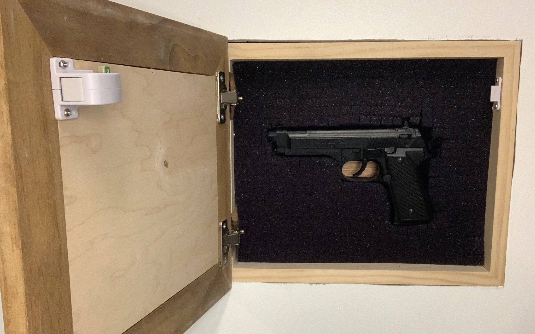 Bellewood Designs recessed hidden gun storage installed in wall, open showing handgun in foam-lined interior with magnetic lock